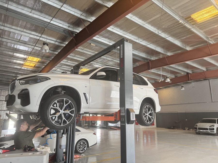 A white BMW X5 raised on a lift while a technician works underneath at BavarLand